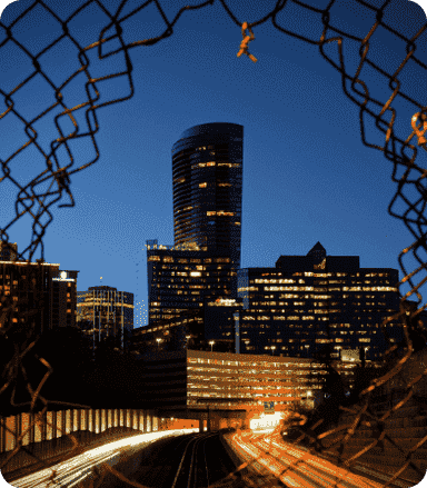 cityscape viewed through hole in chainlink fence